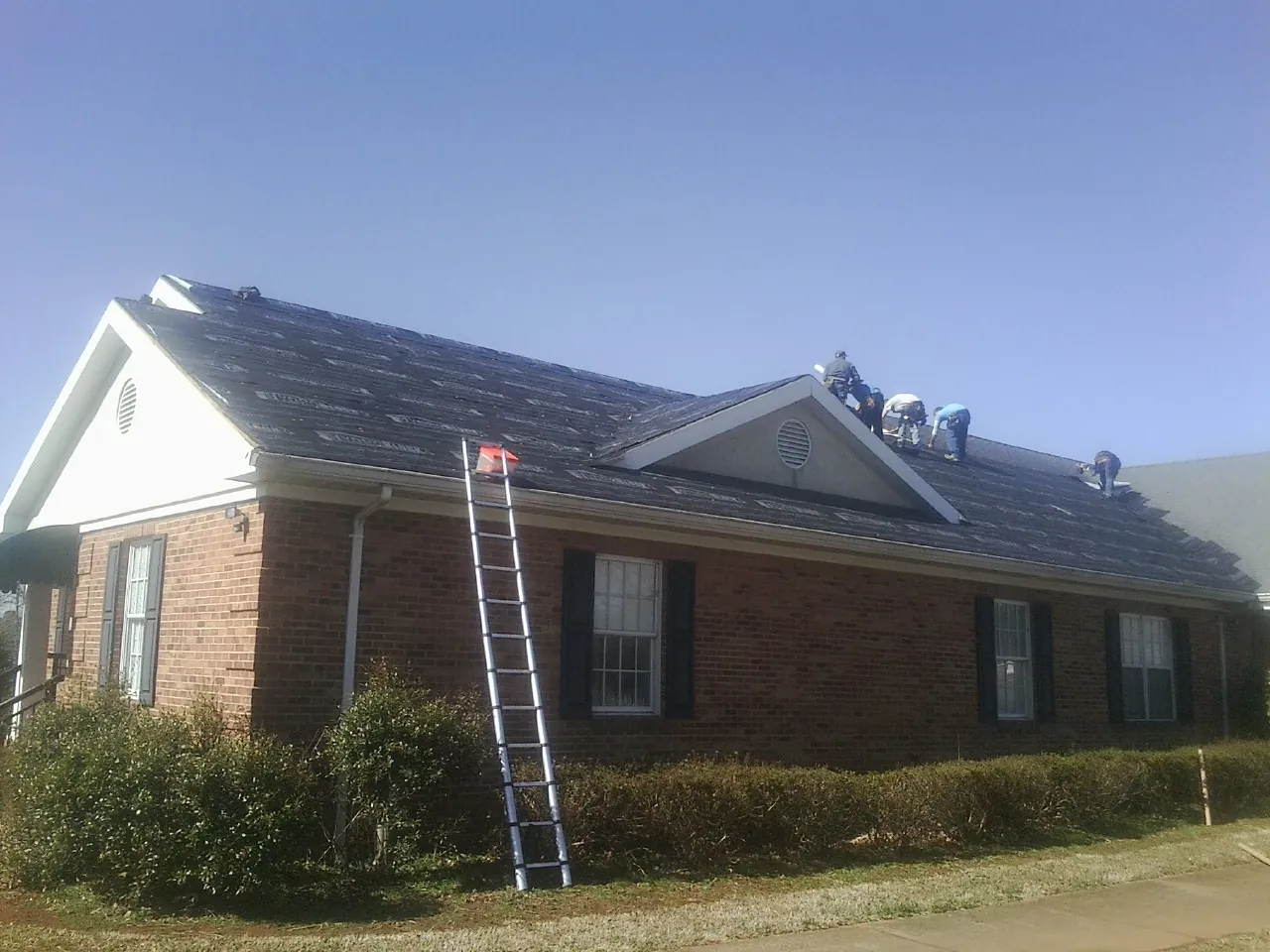 Crew tearing shingles off a brick ranch roof with a ladder set — Emergency Roof Repair work by our crew in Gardners
