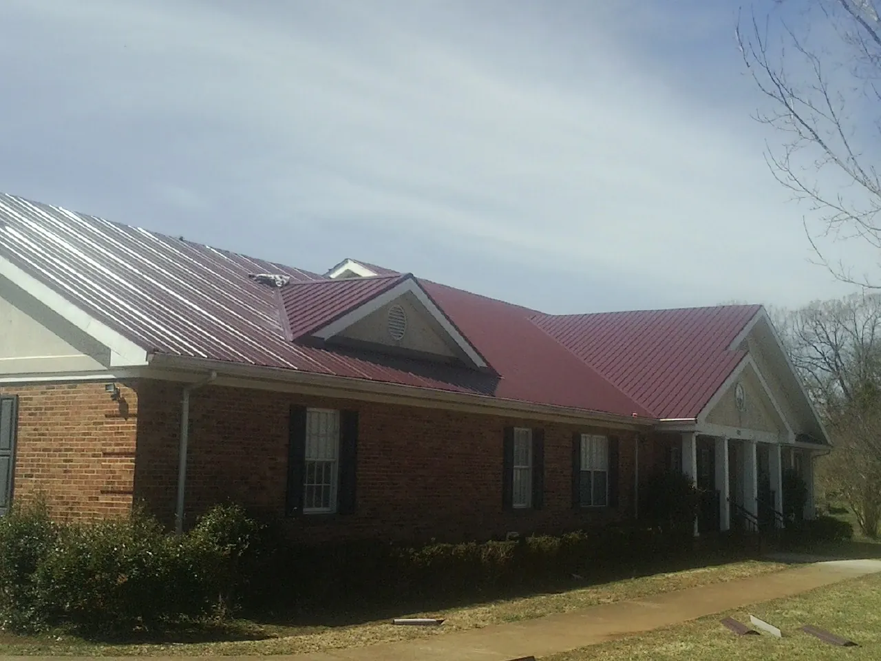 Red metal roof with gabled entries on a long brick building, from a Hail Damage Roof Repair job in Gardners