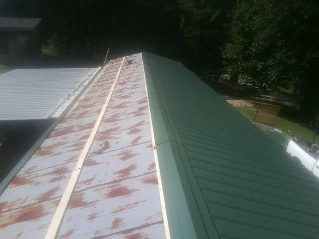 Old rusted panels beside newly installed green metal roofing — Wind Damage Roof Repair by Roofing Brothers in Gardners