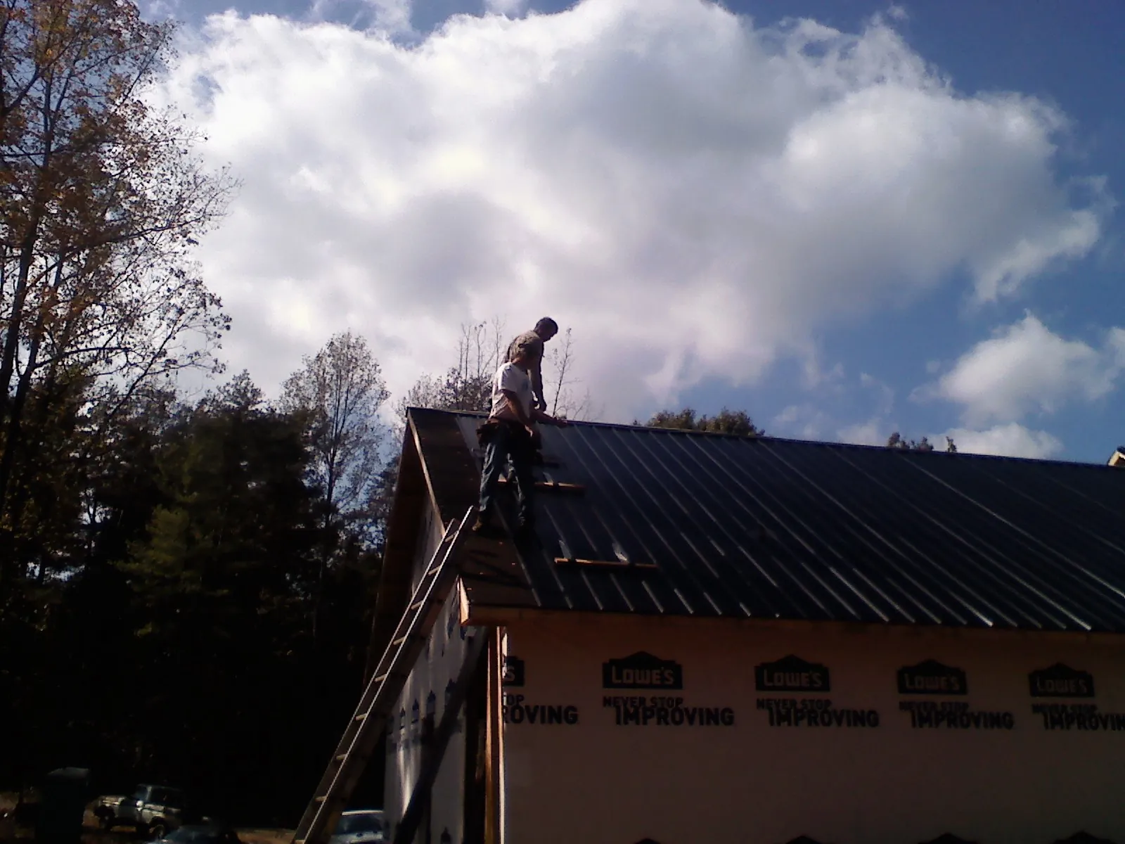Roofer fastening dark metal panels high against a cloudy sky, from a Roof Inspection job in Gardners