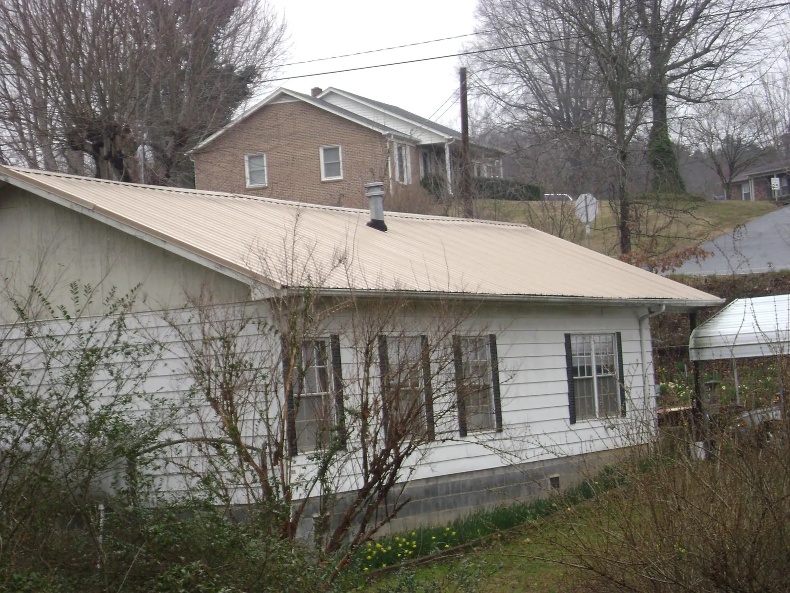 Tan metal roof on a white sided house set into a hillside — Commercial Roofing by Roofing Brothers in Gardners